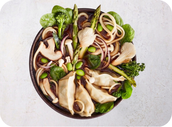 Savory ramen bowl with noodles, dumplings, mushrooms, spinach, asparagus, and edamame.
