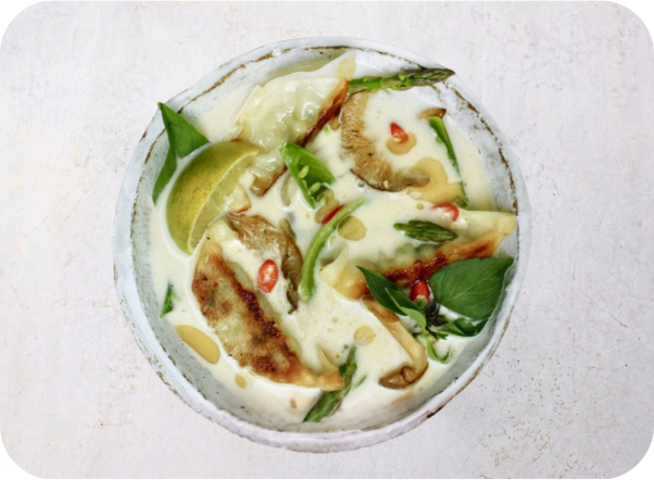 Creamy white soup with pan-fried dumplings, green vegetables, mushrooms, and lime slices.