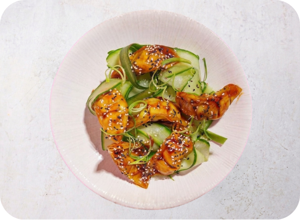 Glazed salmon with cucumber ribbons and sesame seeds in a light bowl.