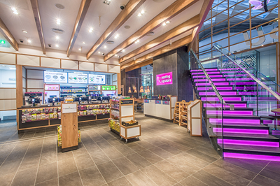 Modern store interior featuring warm wooden decor, a checkout counter, and a staircase with vibrant pink lights.