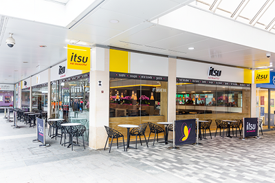 Itsu restaurant exterior with outdoor seating under a prominent yellow and white sign.