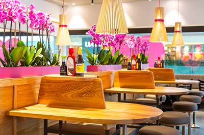 Modern restaurant interior with wooden tables, pink orchids, and hanging pendant lights.