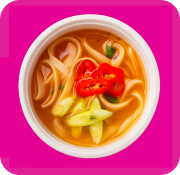 Top view: spicy noodle soup with wide noodles, red chilies, green onions in a white bowl.