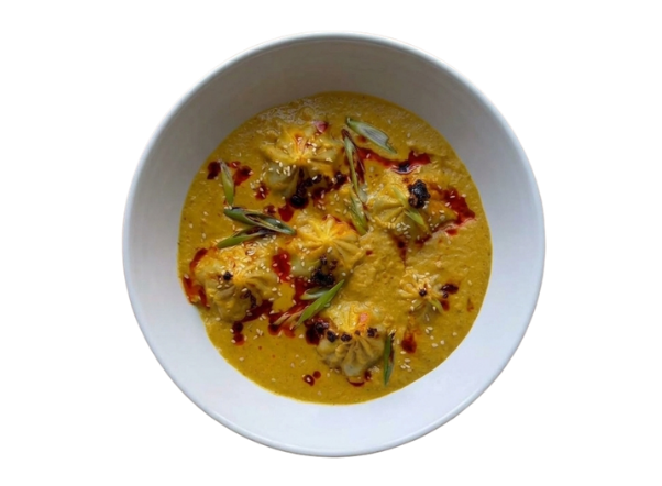White bowl with creamy yellow stew, dumplings, melted cheese, red oil, and scallions.