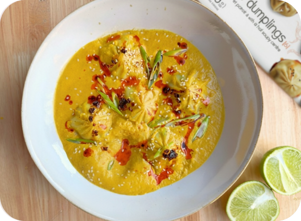 Golden dumplings in creamy yellow sauce with chili oil, green onions, sesame, and fresh lime.