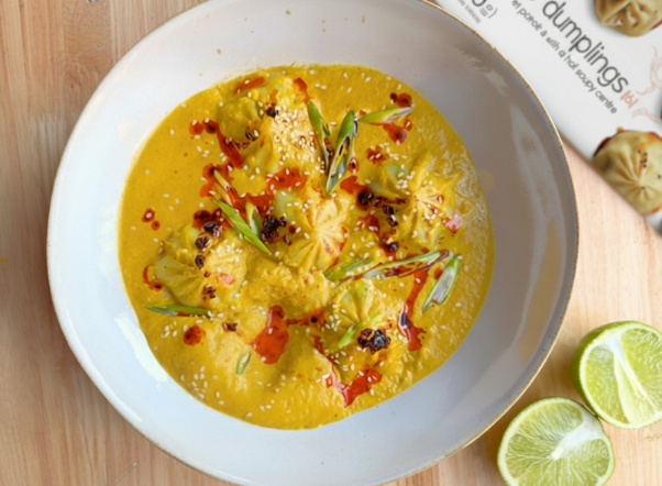 Yellow curry and dumplings in a white bowl, garnished with green onions and chili oil.