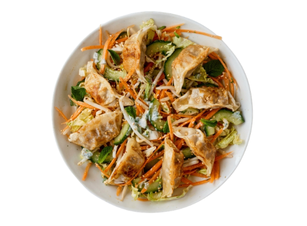A bowl of fresh salad topped with crispy fried dumplings, shredded carrots, and cucumber.