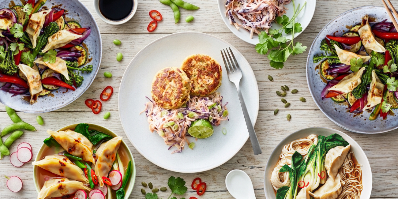Assortment of Asian-inspired dishes on a table, including gyoza, stir-fries, and fish cakes.