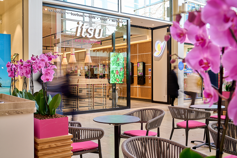 Modern Itsu restaurant in a shopping mall with pink orchids and outdoor seating.