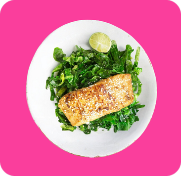 Pan-seared salmon fillet on a bed of saut&eacute;ed collard greens with a lime wedge.