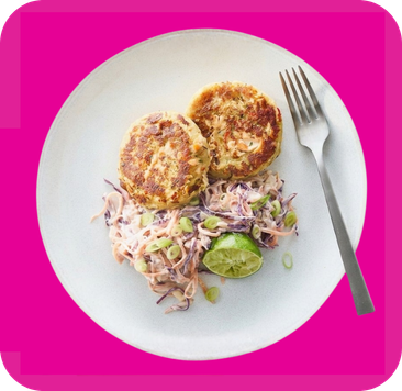 Two golden-brown patties, vibrant coleslaw, and a fresh lime wedge on a white plate.