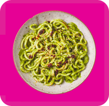 Green curly pasta with pesto sauce and red flakes on a white plate.