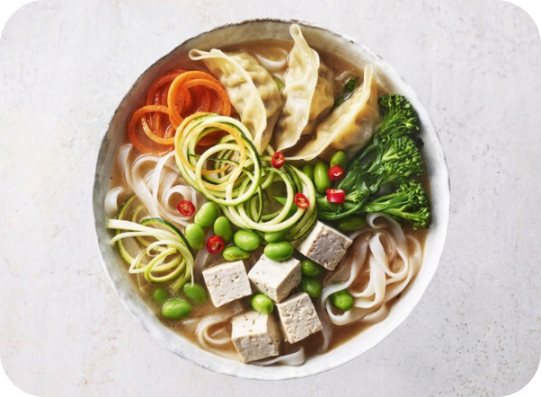 Bowl of miso soup with tofu, noodles, dumplings, broccoli, carrots, and edamame.