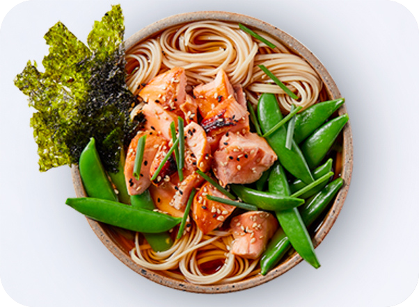 Ramen bowl with salmon, snap peas, seaweed, and chives in a light broth.