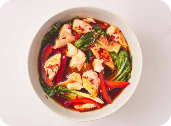 Bowl of pan-seared salmon with bok choy and red chilies in a savory sauce.