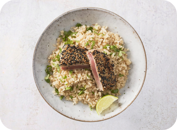 Sesame-crusted seared tuna on cauliflower rice with cilantro and a lime wedge.