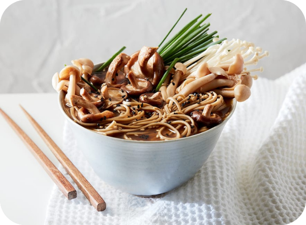 A ceramic bowl of mushroom ramen with chives and chopsticks on a white background.