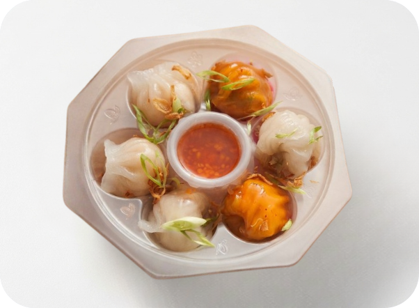 Assorted dim sum dumplings with a central dipping sauce in a hexagonal takeout container.