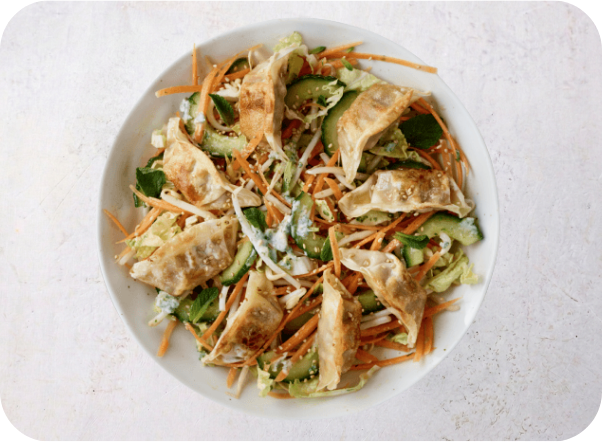 A vibrant Asian-inspired salad featuring fried dumplings, shredded carrots, cucumber, and cabbage.