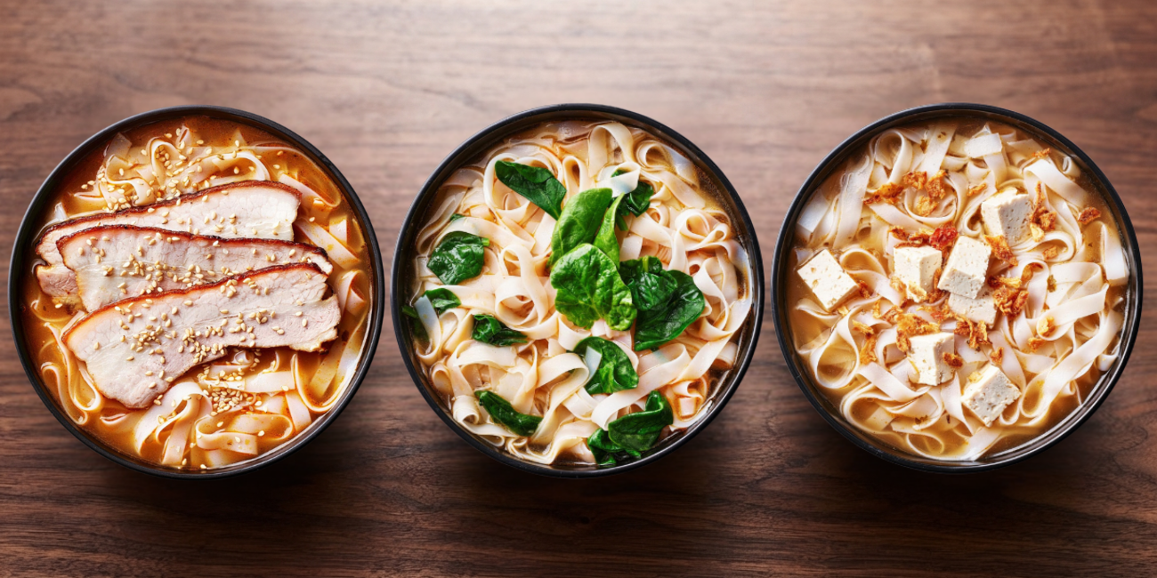 Three Asian noodle soup bowls with pork, greens, and tofu on a dark wooden table.