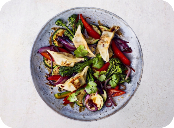 Dumplings and stir-fried vegetables including zucchini, red onion, broccoli, and red peppers on a plate.