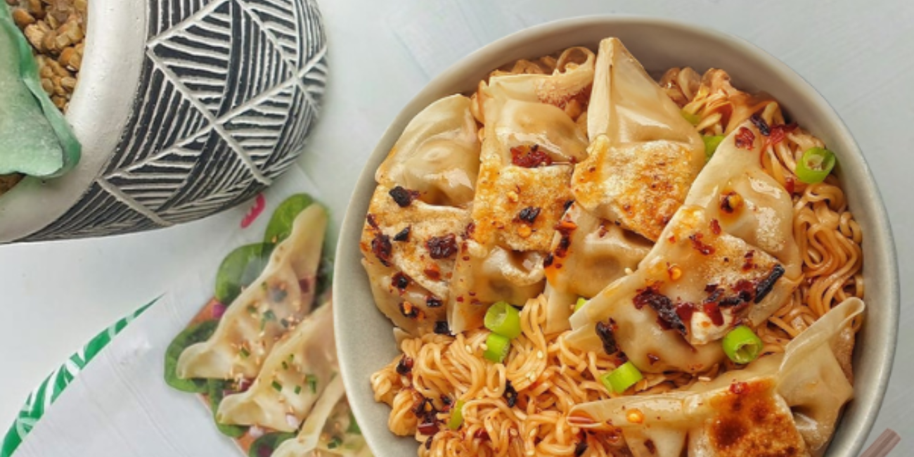 A bowl of pan-fried dumplings with noodles, green onions, and red chili flakes.