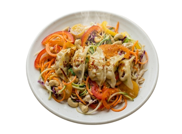 Steaming hot dumplings with colorful spiralized vegetables, bell peppers, and cashews on a white plate.
