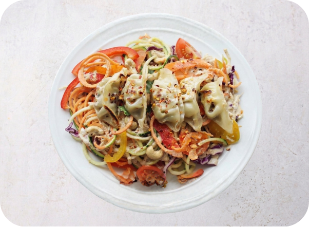 Colorful vegetable noodle salad with dumplings, sliced tomatoes, cashews, and creamy dressing.