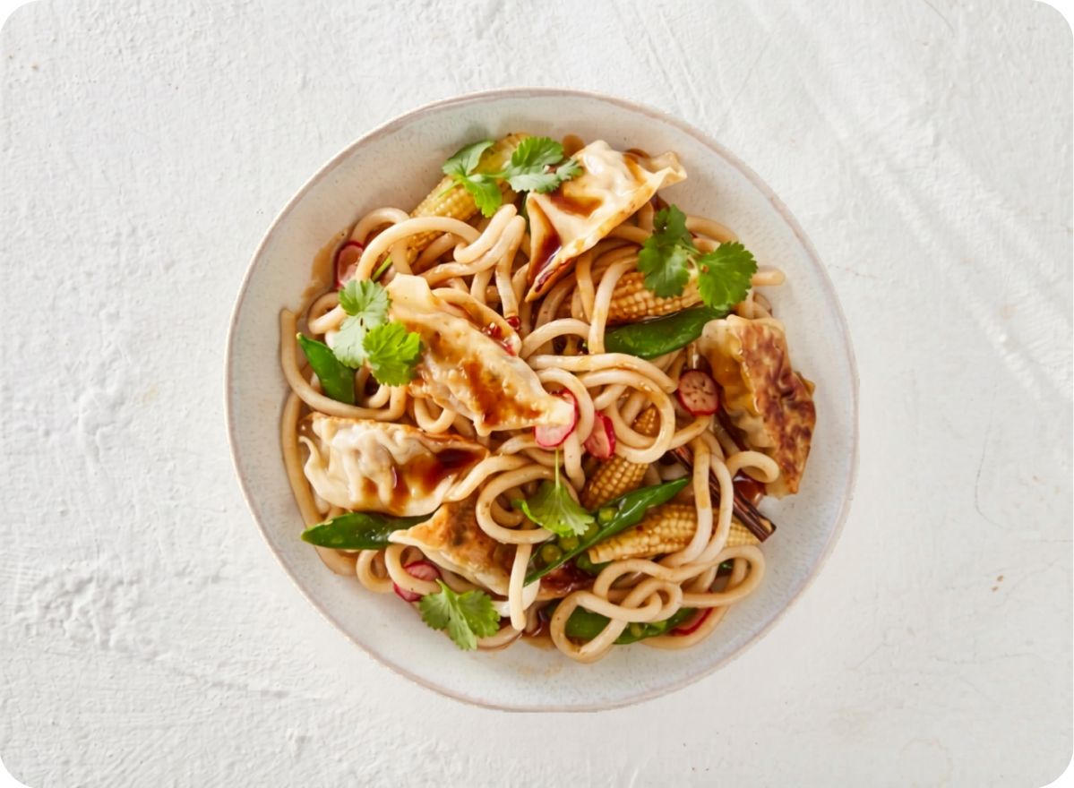 Bowl of stir-fried noodles with pan-seared dumplings, green vegetables, and fresh cilantro.