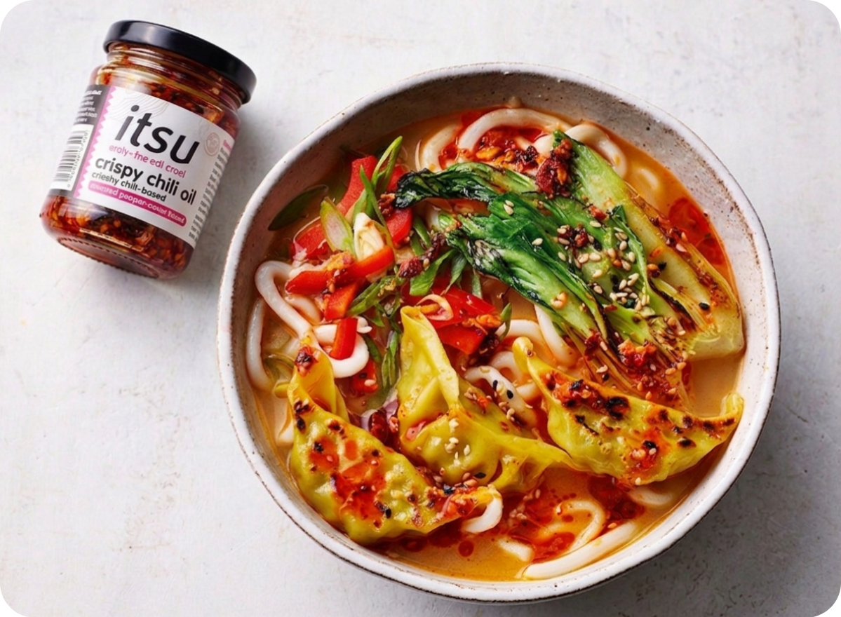 Spicy noodle soup with dumplings, bok choy, and red peppers, drizzled with chili oil.