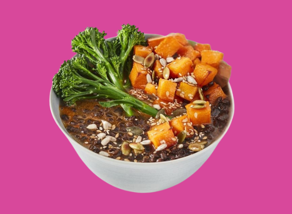 A colorful grain bowl featuring roasted sweet potatoes, broccoli rabe, and mixed seeds.