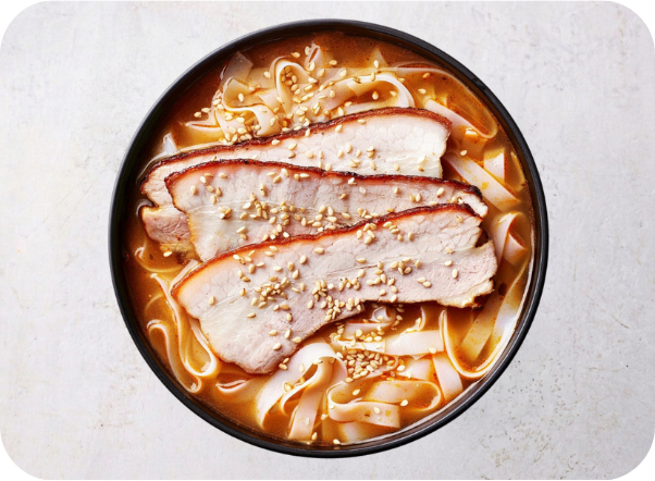 Ramen bowl with pork belly, flat noodles, and sesame seeds in a rich red broth.