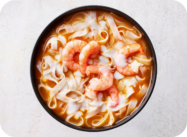 Close-up of a black bowl filled with flat noodles, shrimp, and orange broth.