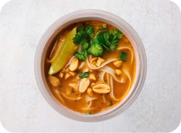 Spicy noodle soup with rice noodles, roasted peanuts, fresh cilantro, and a lime wedge.