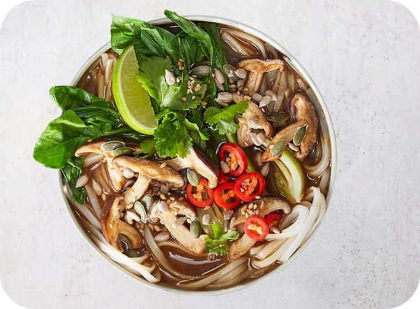 Noodle soup with fresh bok choy, mushrooms, chili, pumpkin seeds, and a lime wedge.