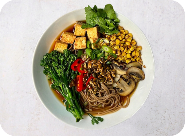 A vibrant bowl of soba noodles with tofu, broccoli, corn, mushrooms, and cilantro.