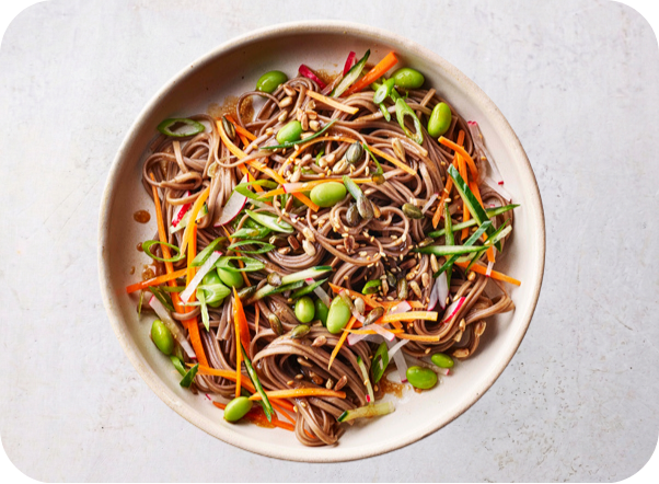 Soba noodle salad with edamame, carrots, cucumbers, and radishes in a ceramic bowl.