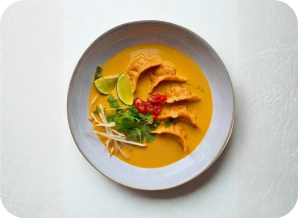 Dumplings in a vibrant yellow curry, garnished with lime, red chili, cilantro, and bean sprouts.