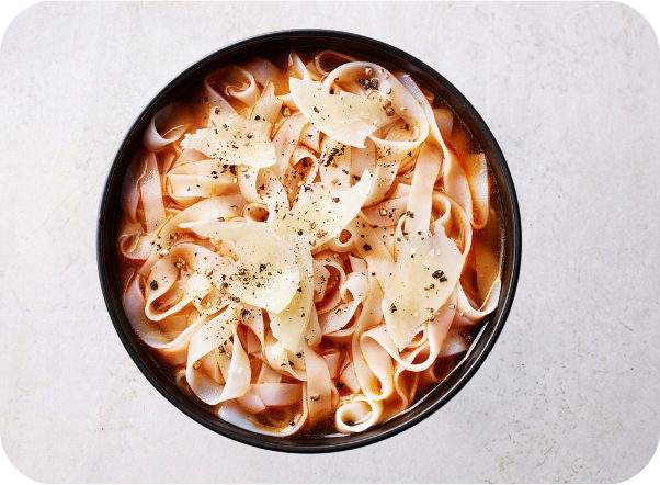 A bowl of tagliatelle pasta topped with shaved parmesan cheese and black pepper.