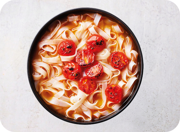 Flat noodles in a rich broth topped with roasted cherry tomatoes in a black bowl.