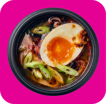 Black bowl of ramen with a soft-boiled egg, sliced green onions, and chili oil.