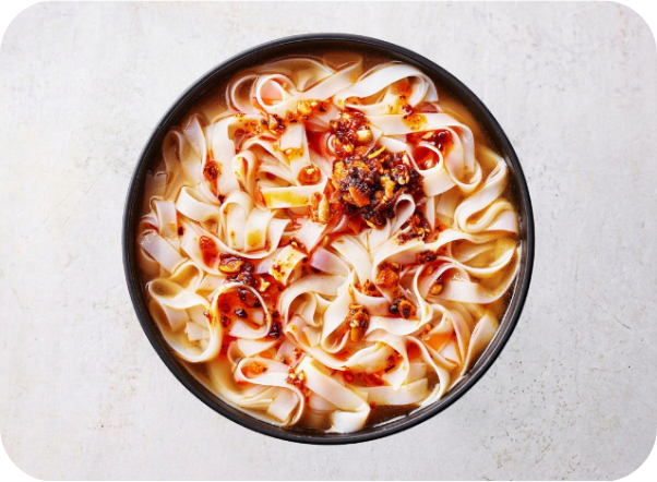 A black bowl of flat white noodles with chili oil and flakes in broth.