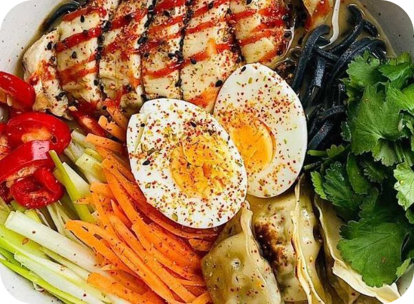 Close-up of a vibrant ramen bowl featuring chicken, egg, black noodles, and fresh vegetables.