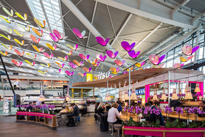 Colorful butterfly decorations hang from the ceiling of a busy airport terminal café.