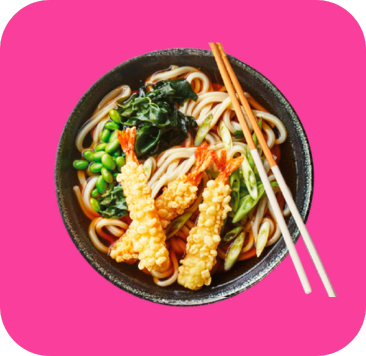 Bowl of Udon noodles with crispy tempura shrimp, edamame, greens, and chopsticks.