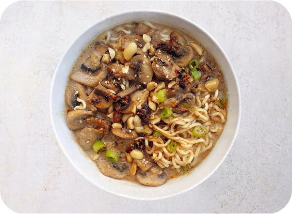 A bowl of savory ramen noodles with mushrooms, peanuts, and green onions in broth.