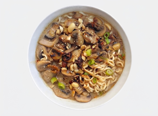 A close-up of a delicious bowl of mushroom ramen with peanuts and green onions.