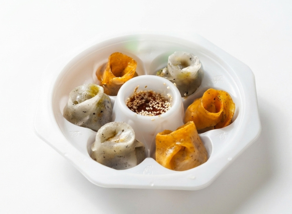 Six colorful spiraled dumplings arranged in a white tray around a central dipping sauce.