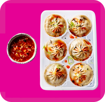 Six pan-fried dumplings garnished with chili oil and sesame, beside spicy red dipping sauce.