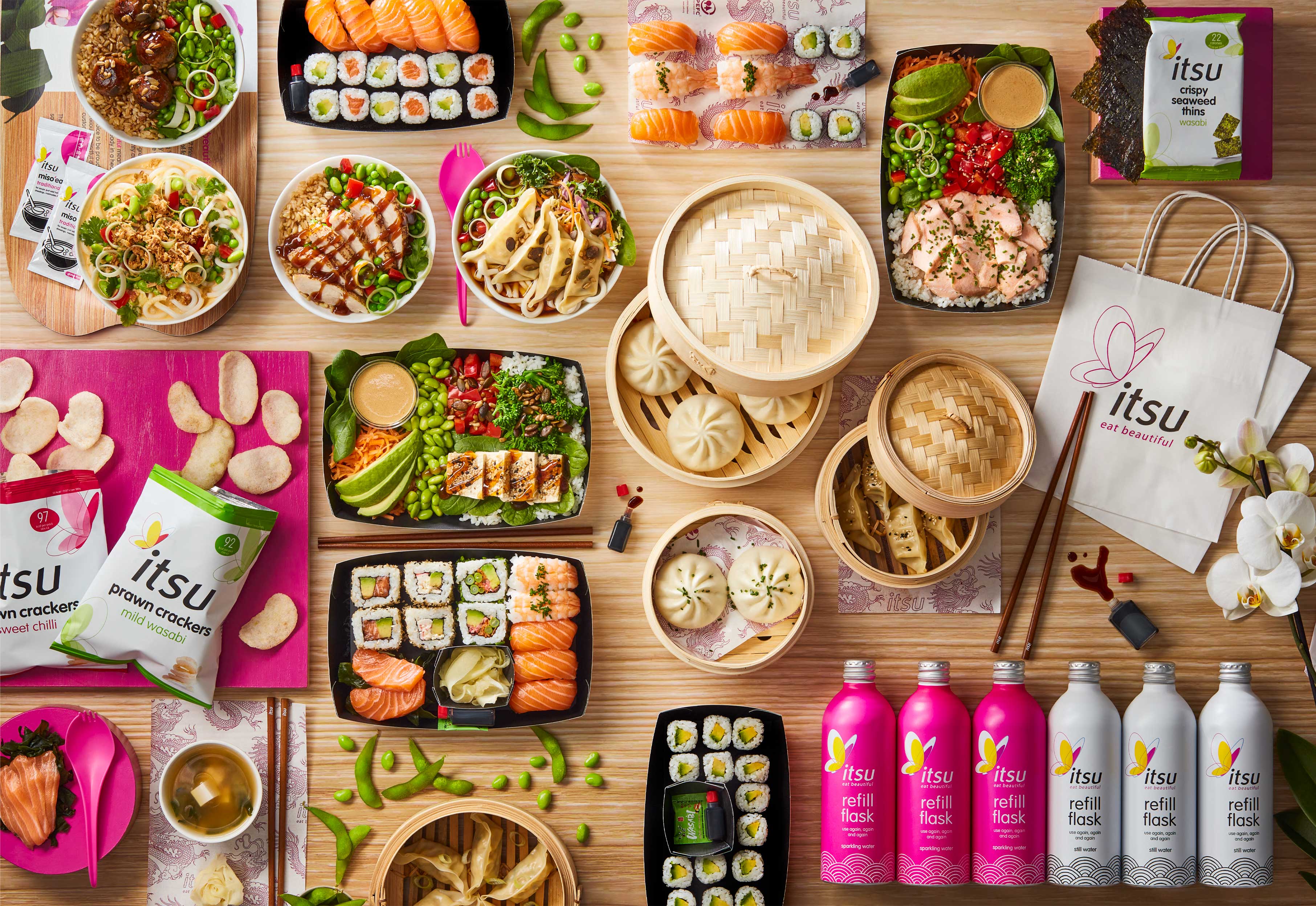 Overhead view of diverse Japanese food, including sushi, dumplings, and salads, by Itsu.